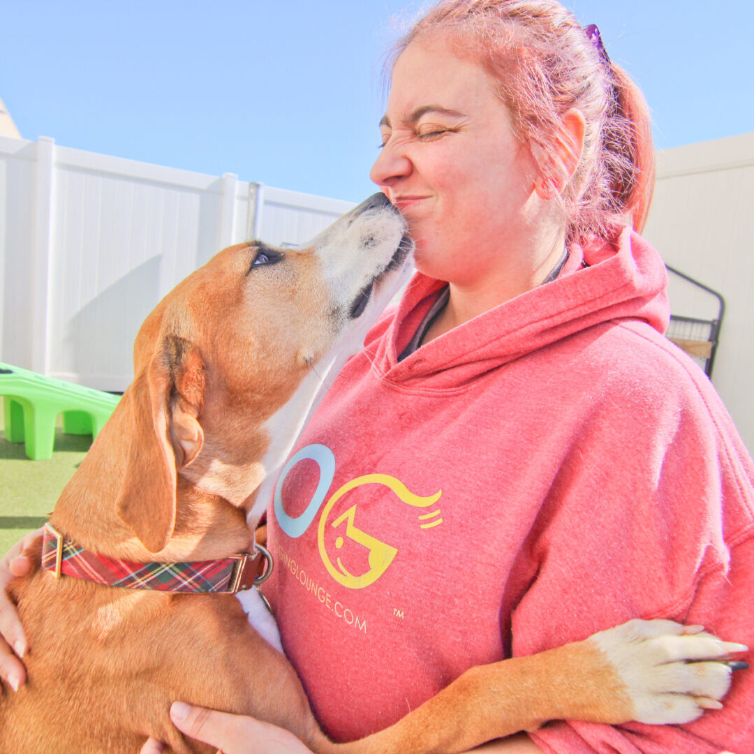 A woman in pink hoodie kissing a brown dog.
